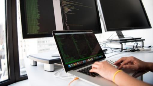 software code displayed on a laptop and computer monitors