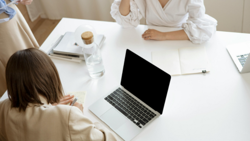 women sitting at white table with black and silver laptop