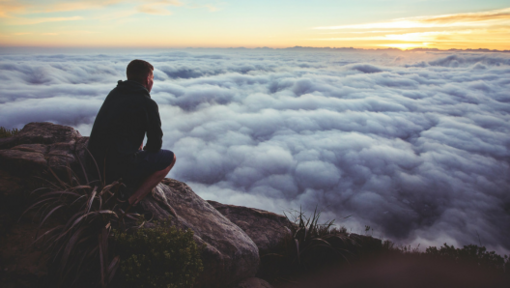 hiker on rock looking out over clouds