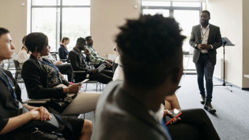 people sitting in chairs in conference room listening to man speaking